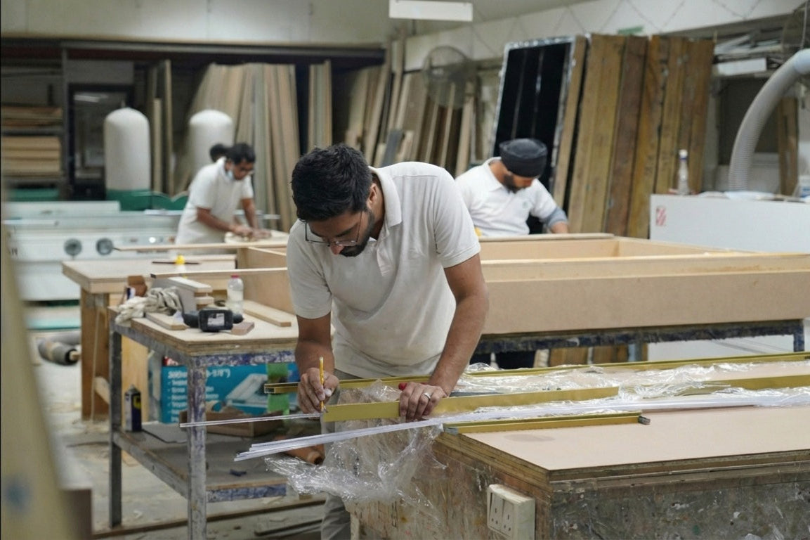 Man measuring wood in a workshop with other workers in the background